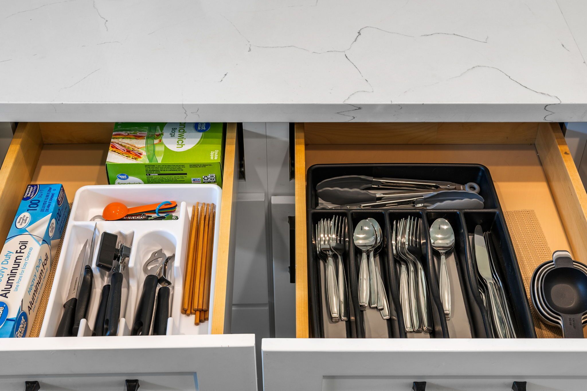 A drawer with kitchen utensils and aluminum foil boxes.