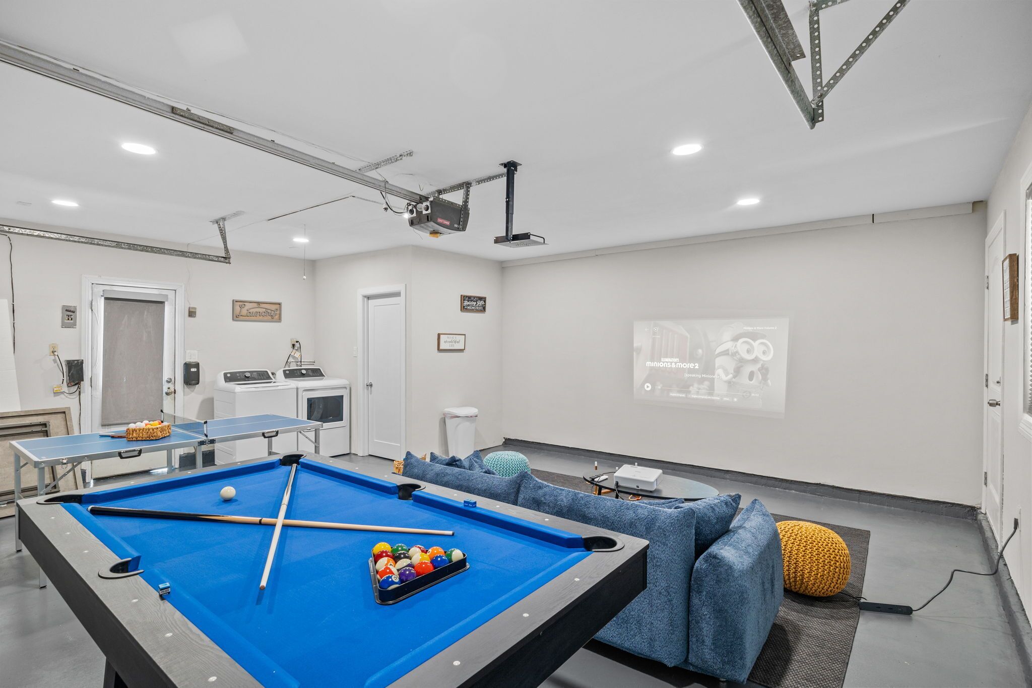 Une pièce équipée d’une table de billard, d’un écran de projection et d’un coin salon avec des canapés.