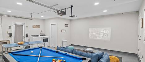 Une pièce équipée d’une table de billard, d’un écran de projection et d’un coin salon avec des canapés.