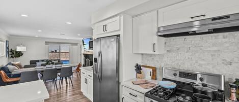 A modern kitchen with stainless steel appliances, white cabinetry, and a dining area with a wooden table and chairs.