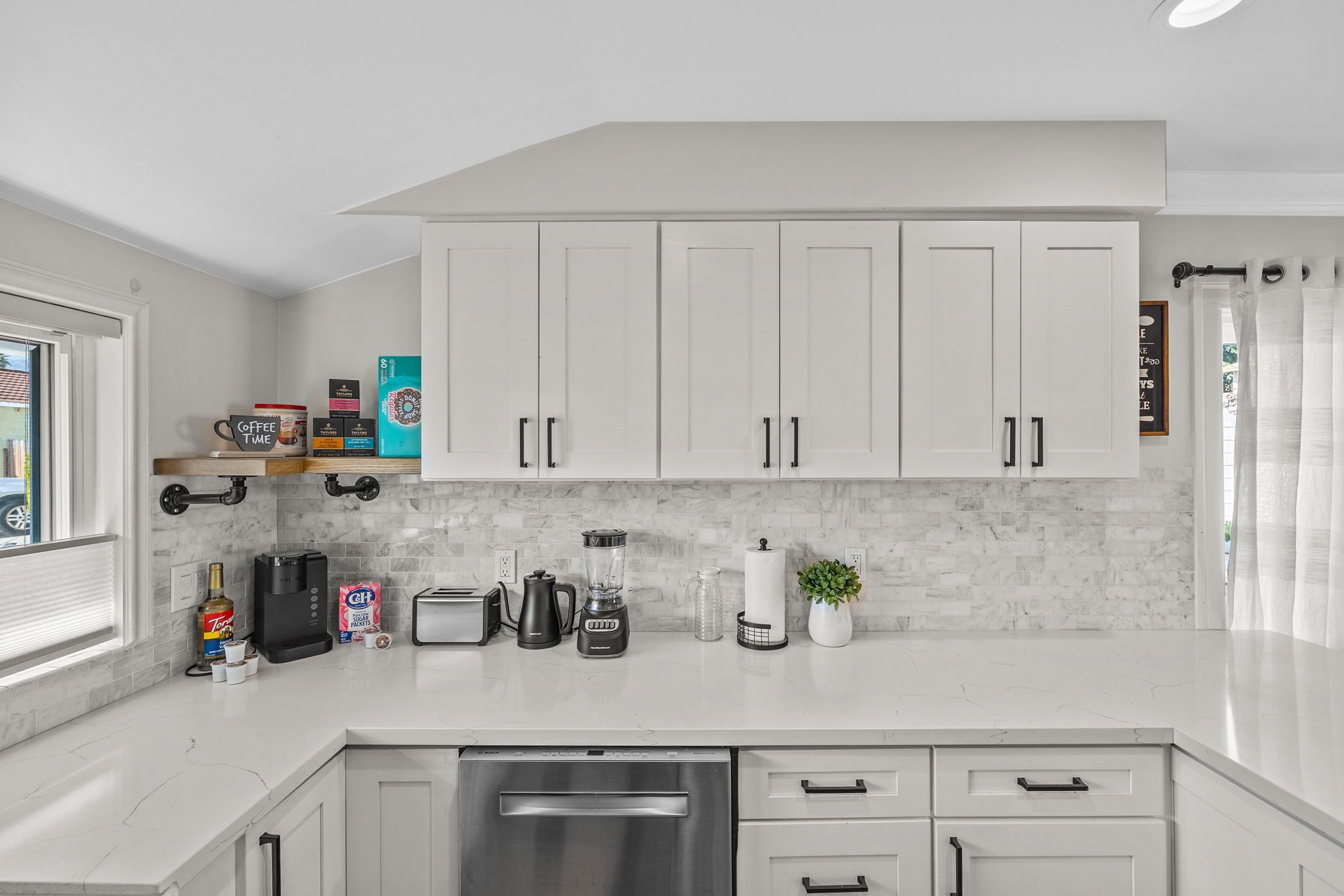 A modern kitchen with white cabinets, a marble countertop, and various appliances like a coffee maker, toaster, and blender.