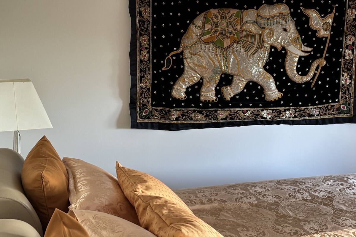 A bedroom with a bed, a nightstand, a lamp, and a tapestry of an elephant.