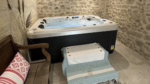 Una habitación con pared de piedra, una silla de madera, un tapete de baño a rayas y una bañera de hidromasaje con agua corriente.
