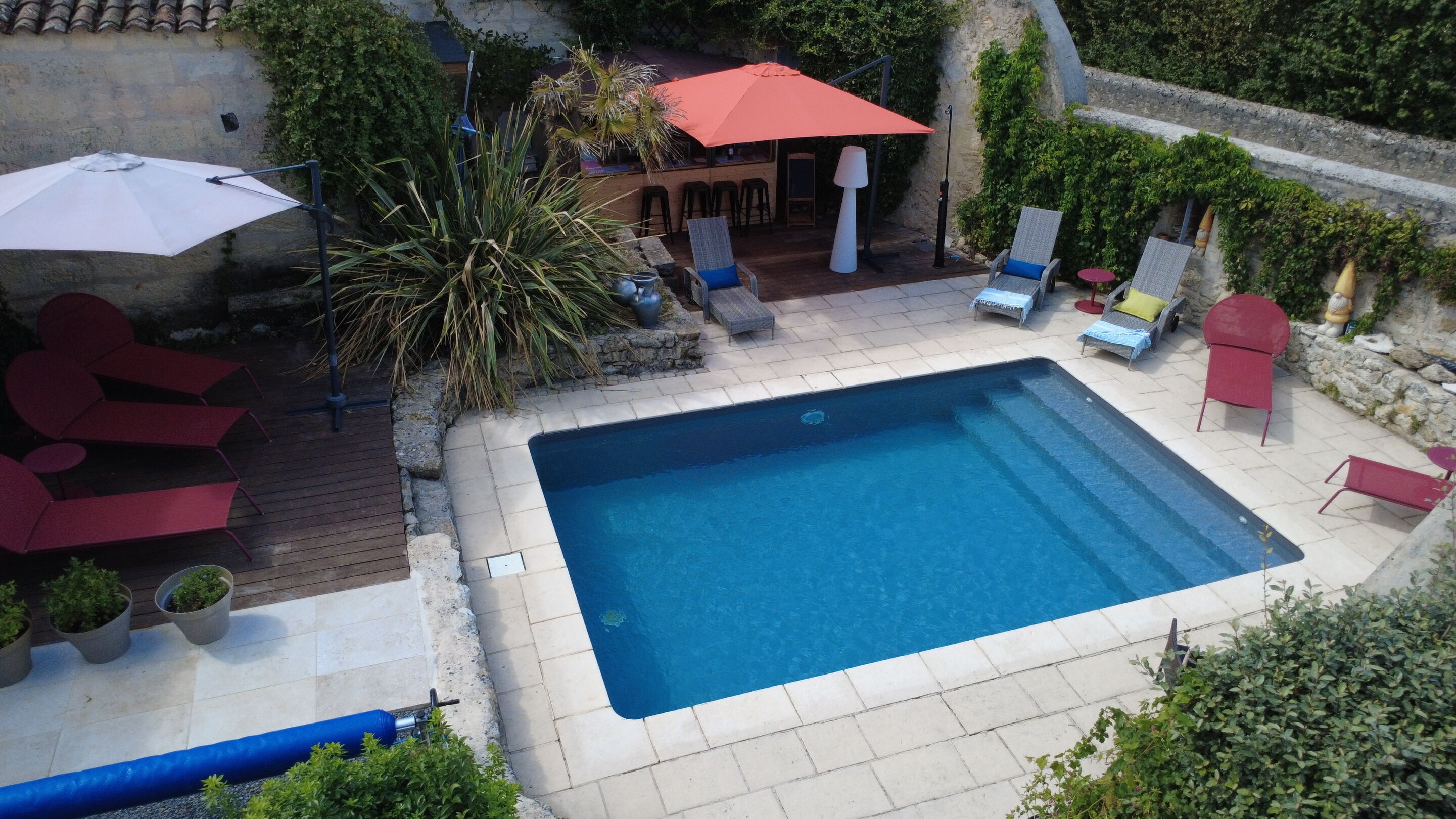 A rectangular swimming pool with a tiled deck, surrounded by lounge chairs and umbrellas.