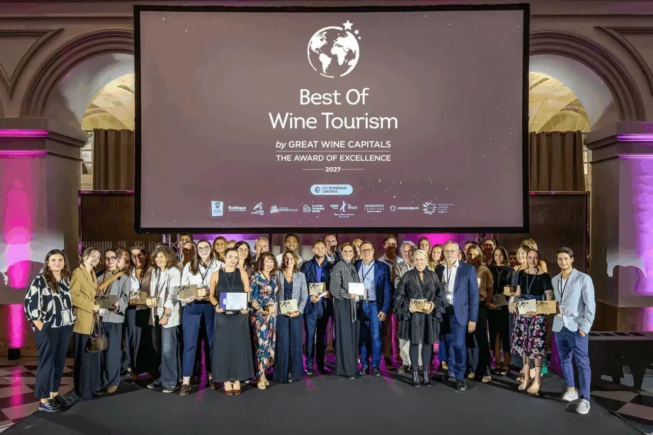 A group of people on a stage with a screen displaying 'Best Of Wine Tourism by GREAT WINE CAPITALS THE AWARD OF EXCELLENCE 2027'.
