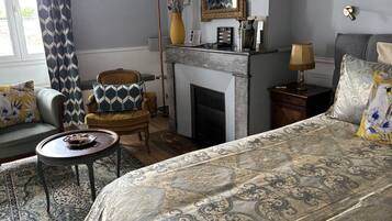 A room with a bed, a sofa, a chair, a small table, a fireplace, and a mirror.