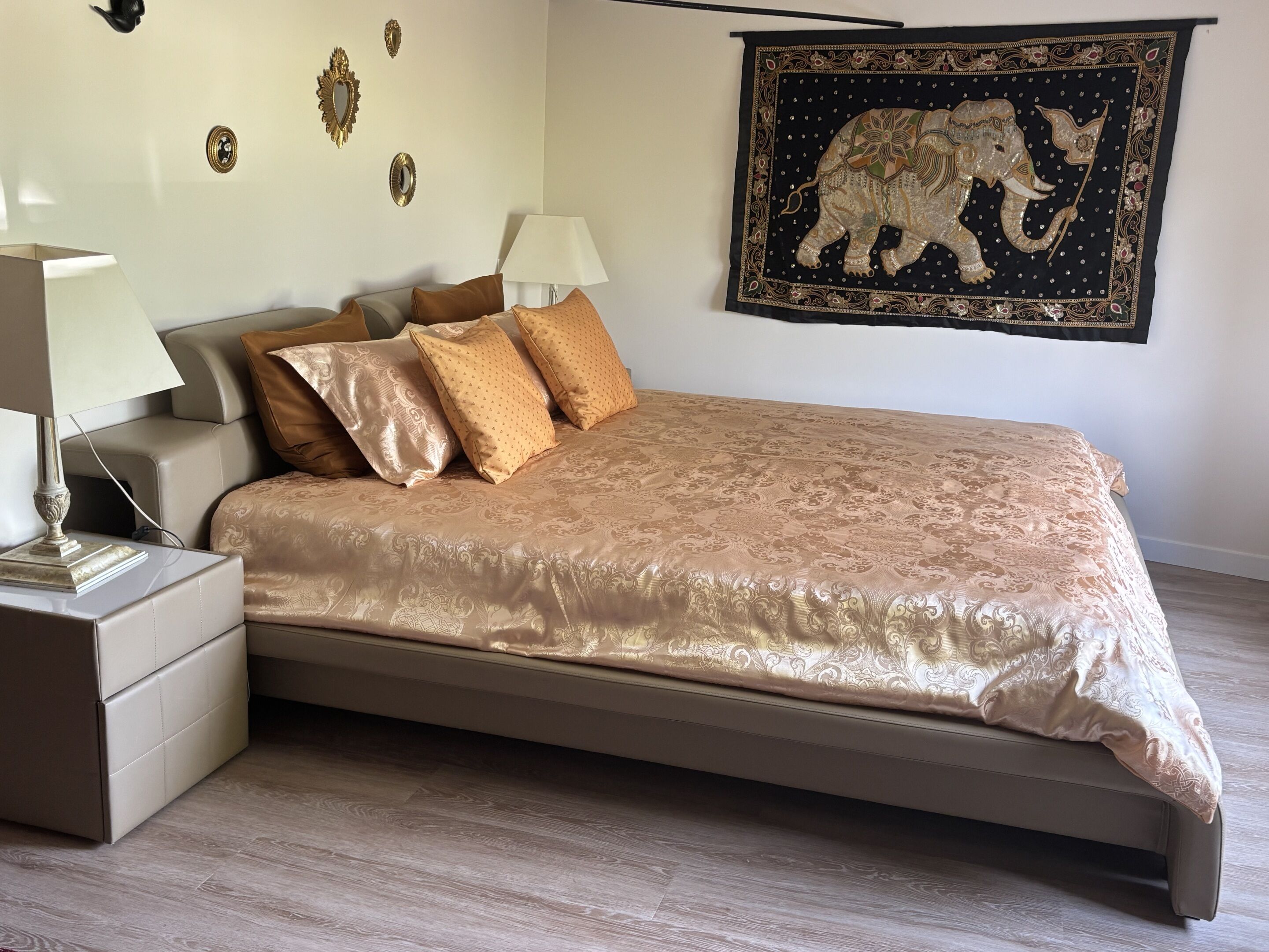 Une chambre à coucher avec un lit, des oreillers, une table de chevet, une lampe, une tapisserie et des éléments de décoration murale.