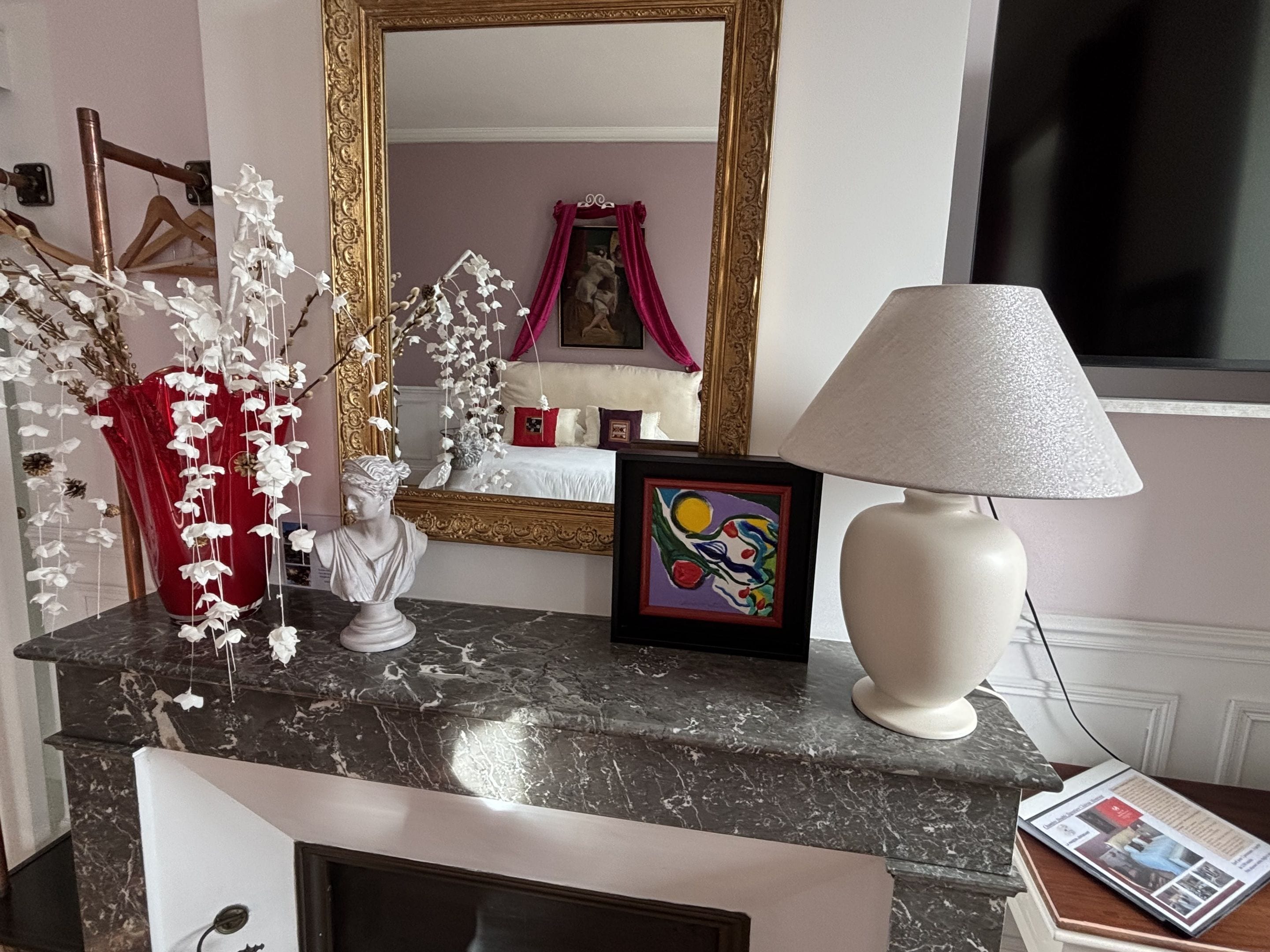 A marble countertop with a white lamp, a framed painting, and a vase with white flowers.