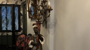 Una habitación con una gran lámpara de araña ornamentada, un sillón estampado y un espejo decorativo.