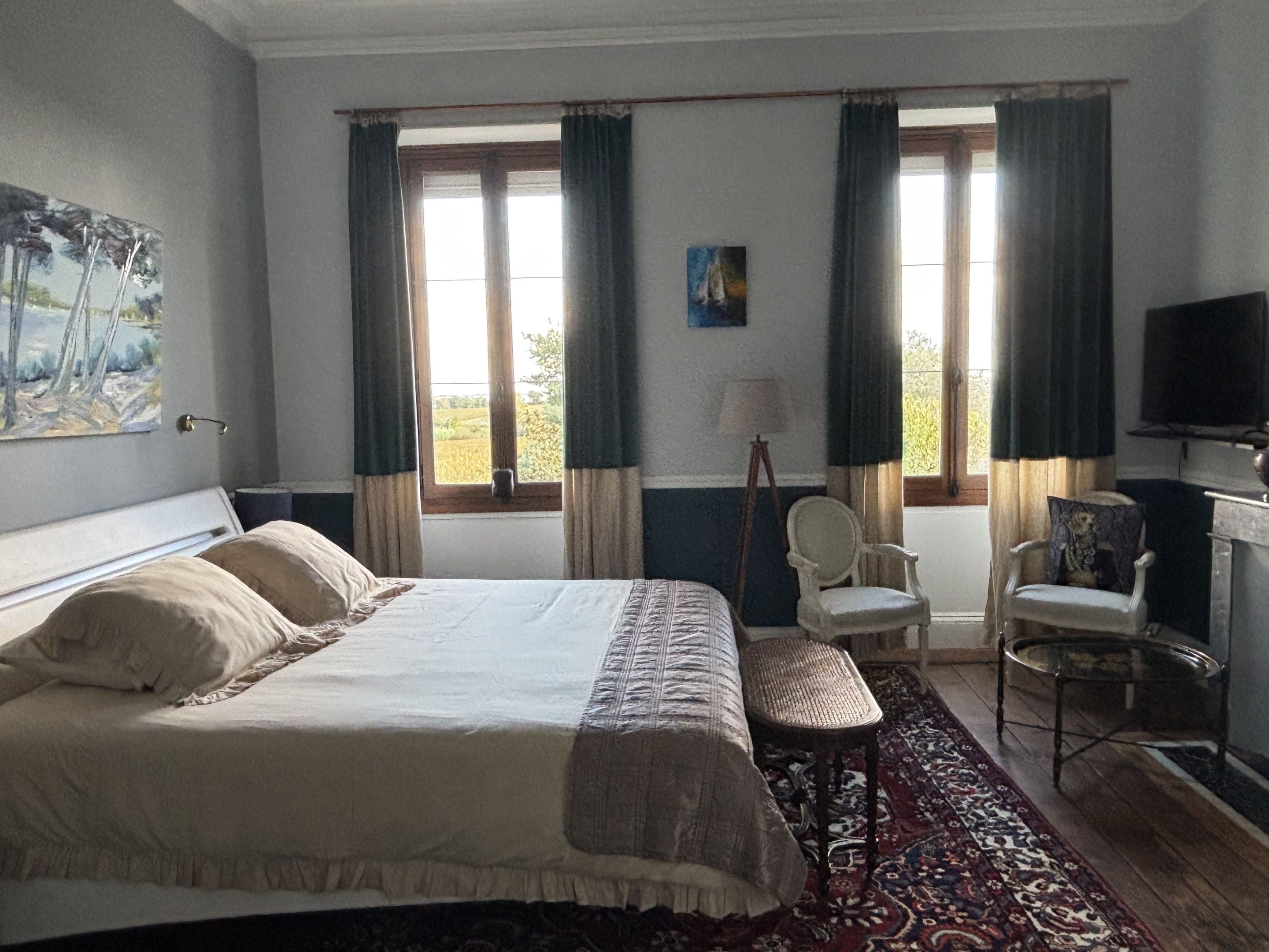Een slaapkamer met een bed, twee stoelen, een televisie en een raam met gordijnen.