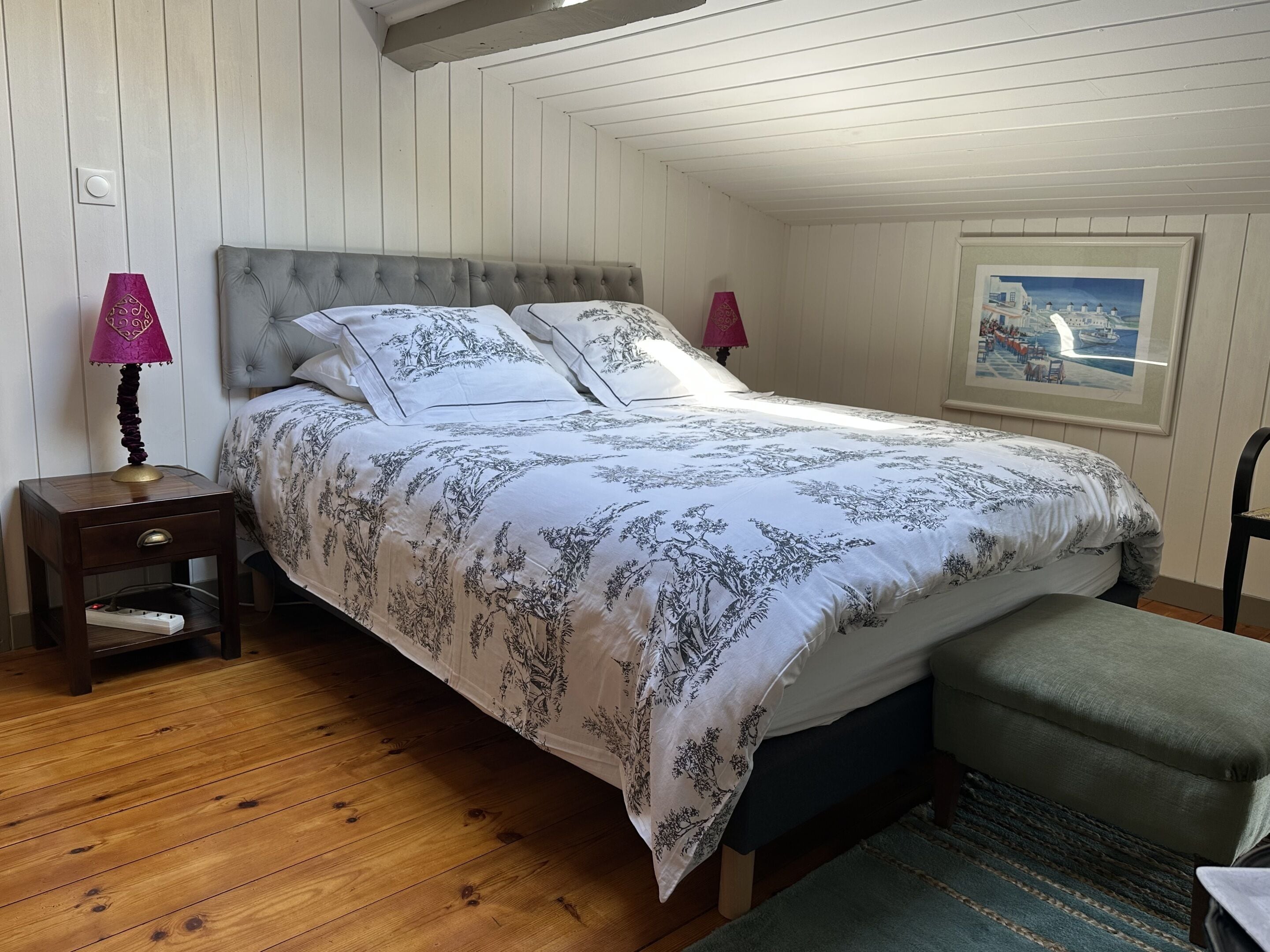 Une chambre à coucher avec un lit, des tables de chevet, une lampe, une chaise, un tapis et un tableau au mur.