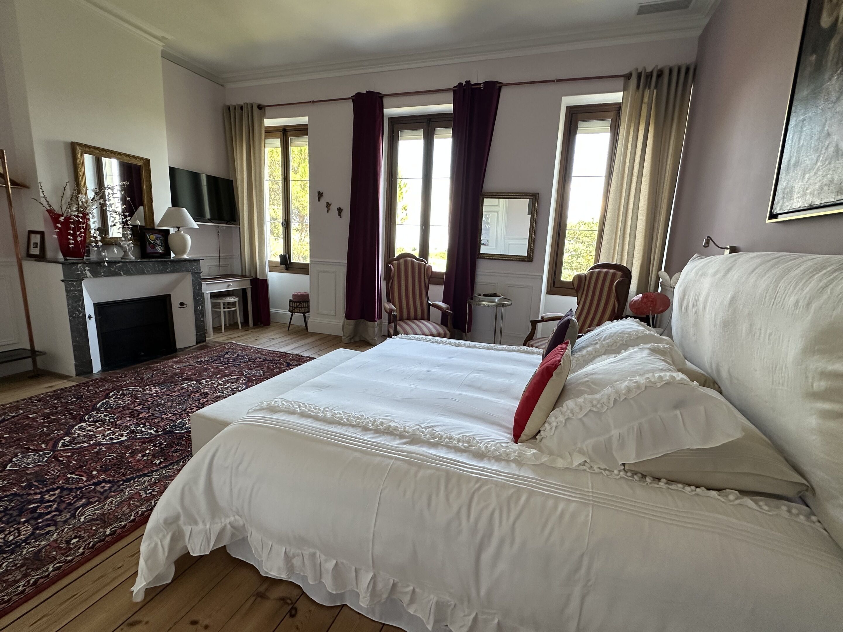 Une chambre avec un grand lit, une cheminée, un bureau et deux chaises.