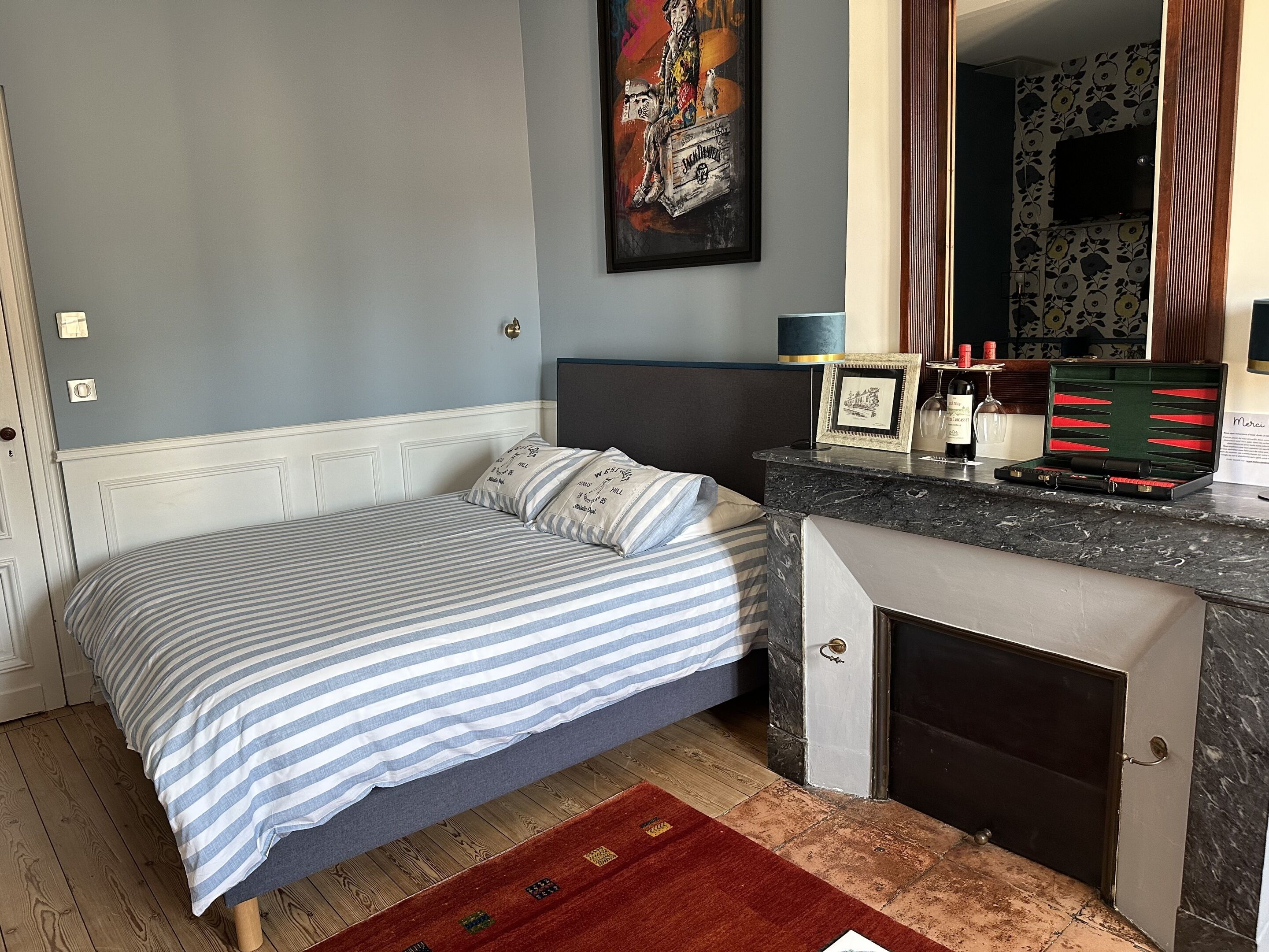 Un dormitorio con cama, cómoda, espejo y chimenea.