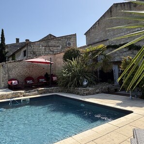 A swimming pool with a stone wall, outdoor seating, and a palm tree. - Maison Jéroboam (Saint-Estephe)