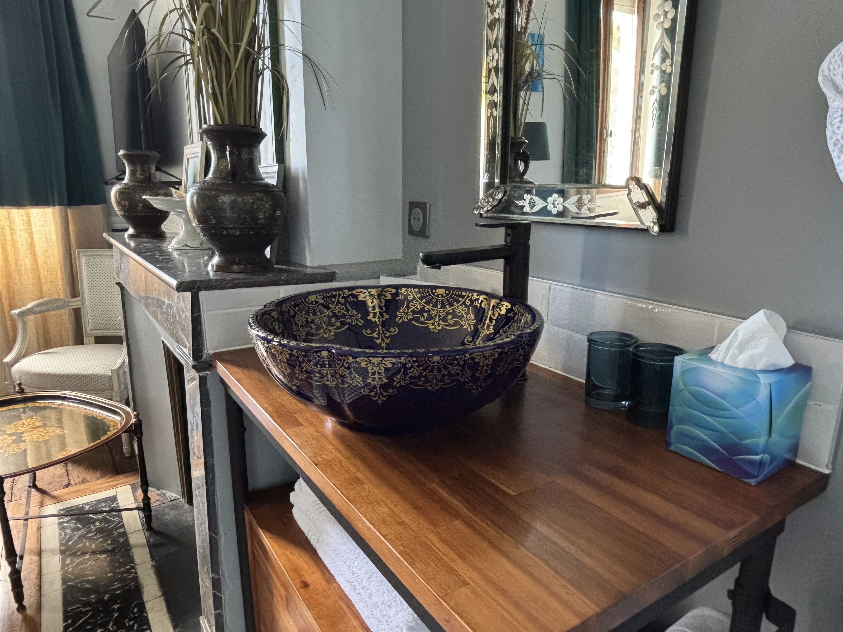 Un baño con un recipiente decorativo grande sobre un mostrador de madera, un espejo encima, un dispensador de toallas y una caja de pañuelos.