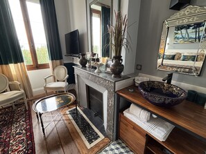 A room with a fireplace, a large mirror, a bowl sink, and a television. - Maison Jéroboam (Saint-Estephe)