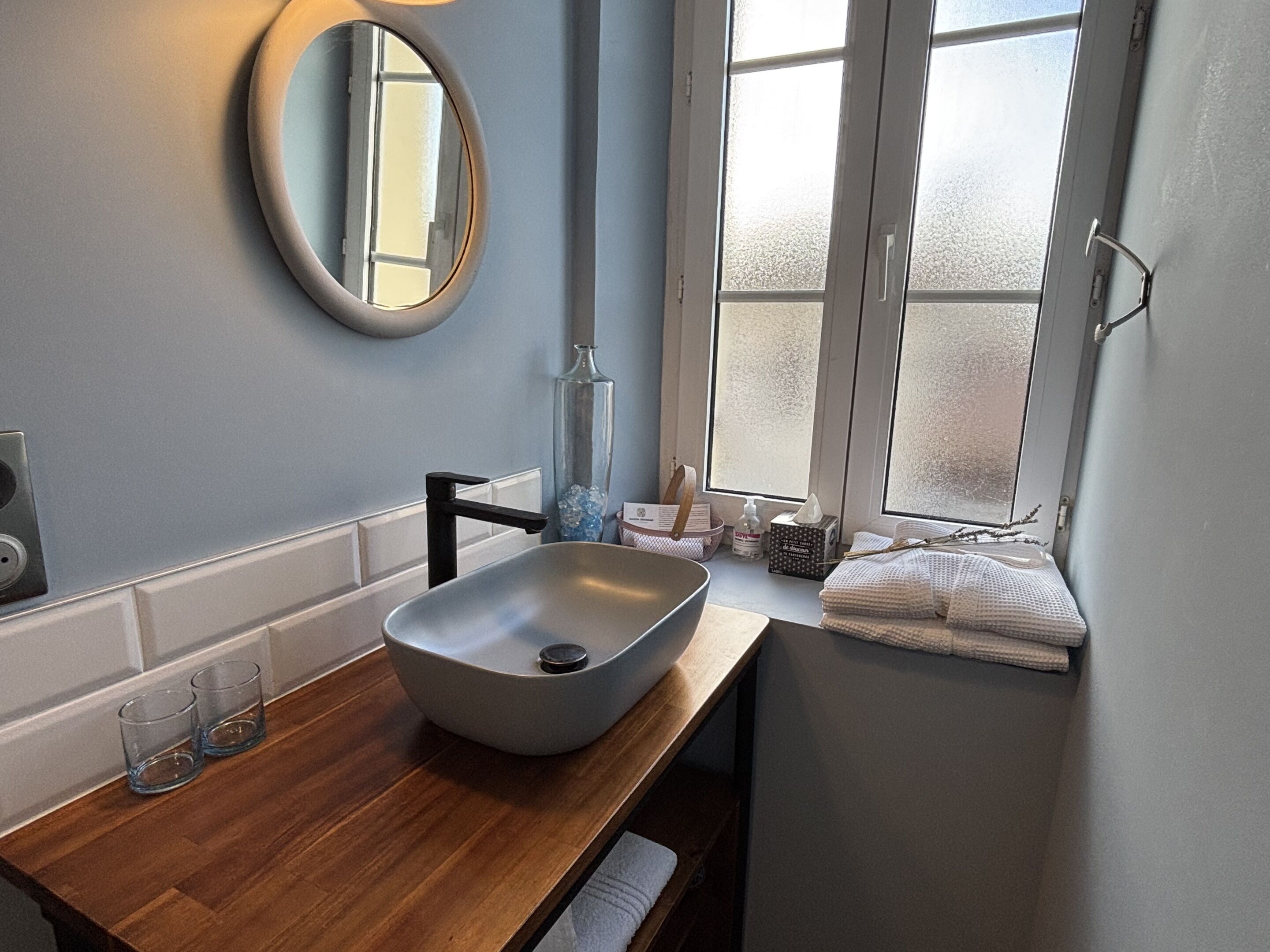 Une salle de bain avec un meuble-lavabo en bois, un vasque, un miroir et une fenêtre en verre dépoli.