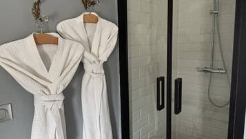 Een badkamer met twee witte badjassen aan een muur, een douchecabine van glas en een handdoekhouder met een decoratief object.
