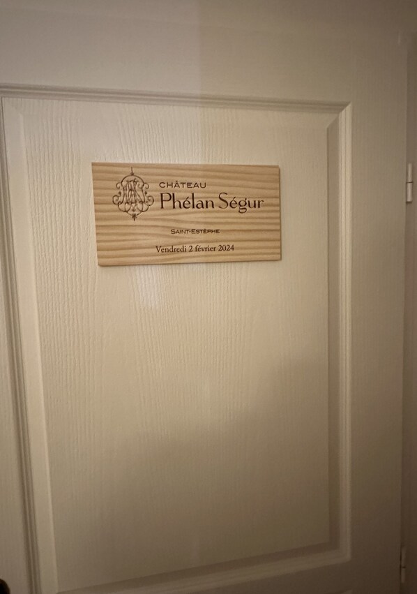 Una placa de madera con el texto "CHÂTEAU Phélan Ségur" y "SAINT-ESTEPHE" en una puerta blanca.