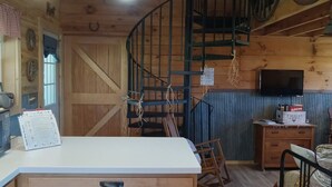 A rustic interior with a wooden staircase, a white counter, and a television on a wooden cabinet.