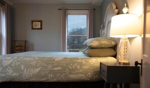 A bedroom with a bed, a nightstand, a lamp, a window, and a picture on the wall.