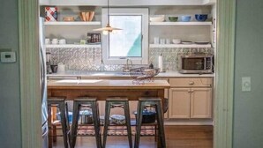 A dining area with a wooden table and chairs, a kitchen in the background with a microwave and cabinets, and a hanging light fixture. - Berkshire House Stay: 5BR/5BA (Lee)