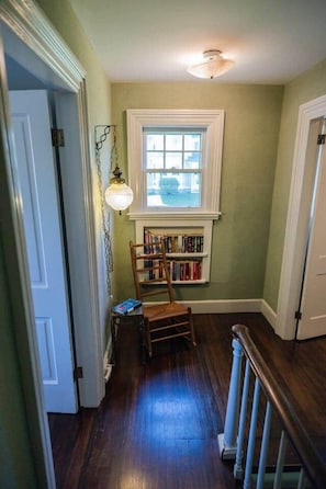 Un pasillo con una silla de madera, una estantería y una ventana con vistas.