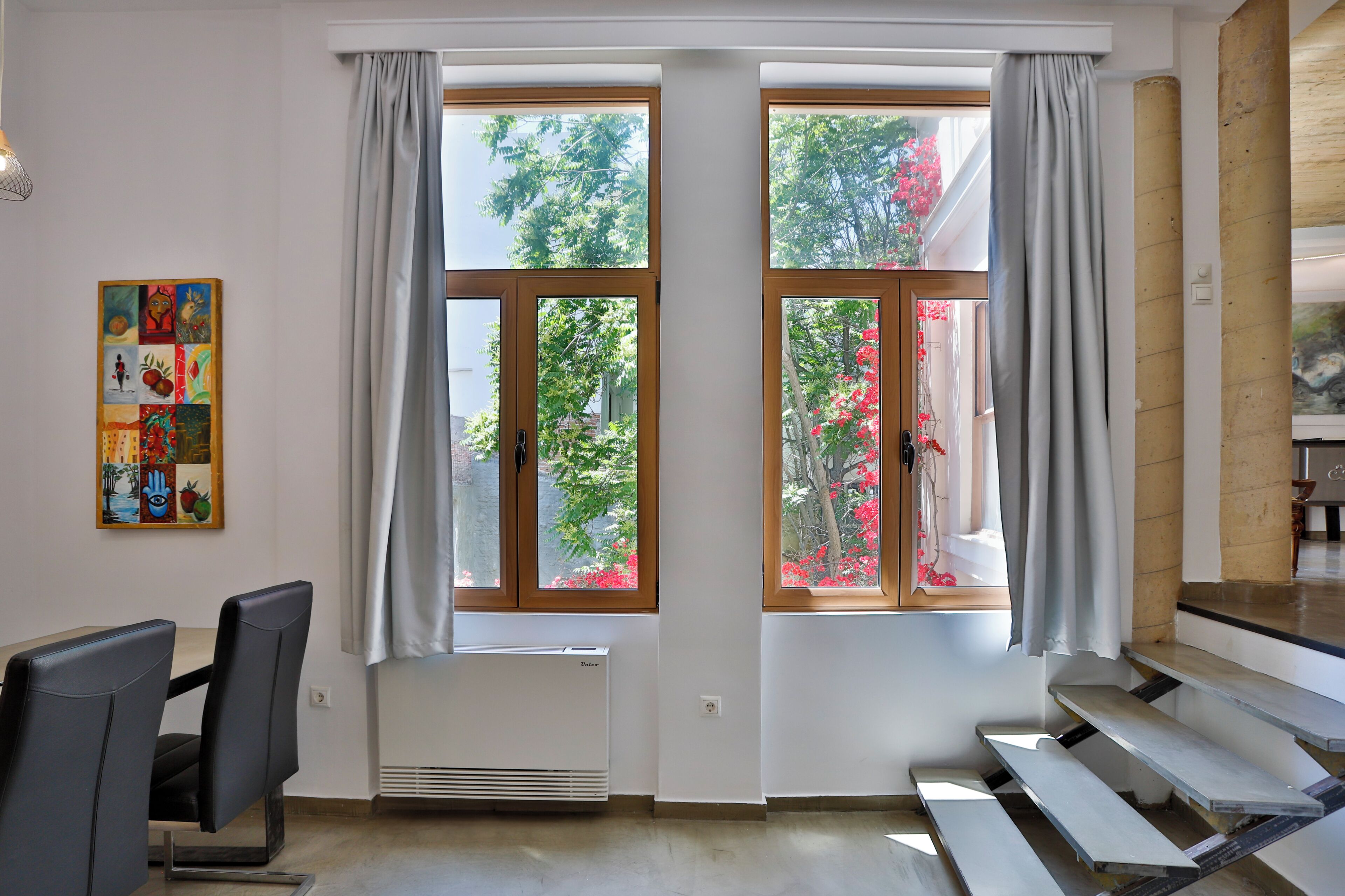Habitació amb taula de dinar, cadirees, radiador i finestres grans amb cortines.