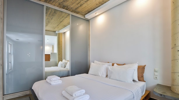 Moderni hotellihuone, jossa on suuri sänky, liukuovilla varustettu vaatekaappi ja ikkunan vieressä oleva puinen penkki.