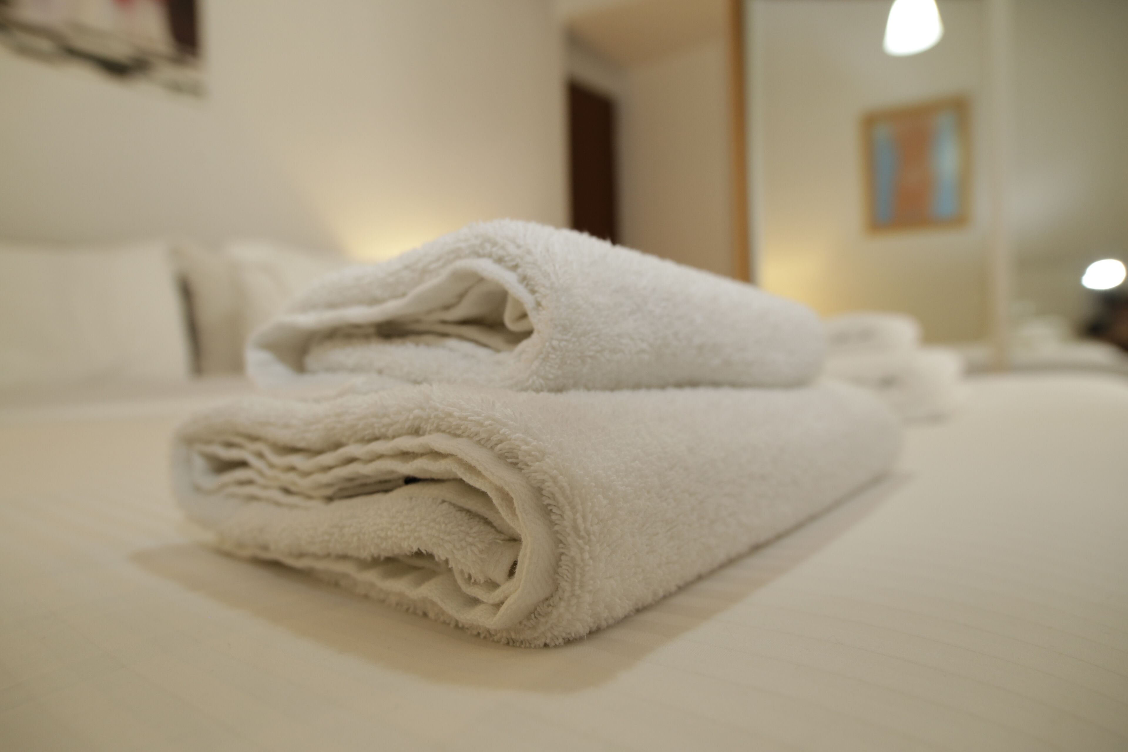 A neatly folded white towel on a bed in a hotel room.