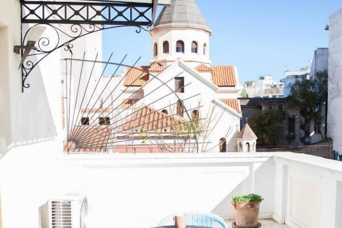 Un balcon avec une table et des chaises, un pot de fleurs et une vue sur un immeuble doté d’une tour.