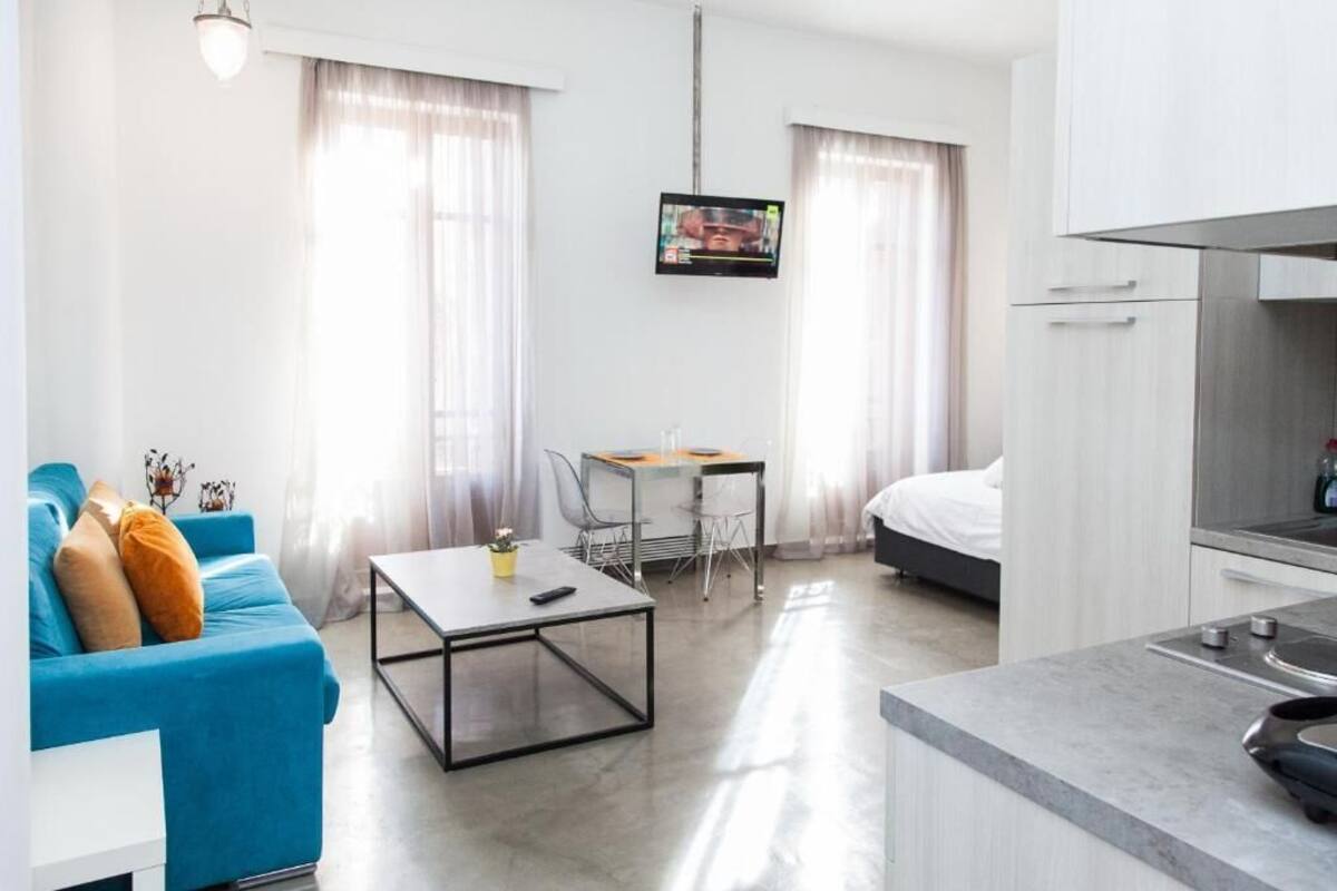 Une chambre d’hôtel moderne avec un canapé bleu, une petite table à manger, un lit et un coin cuisine.