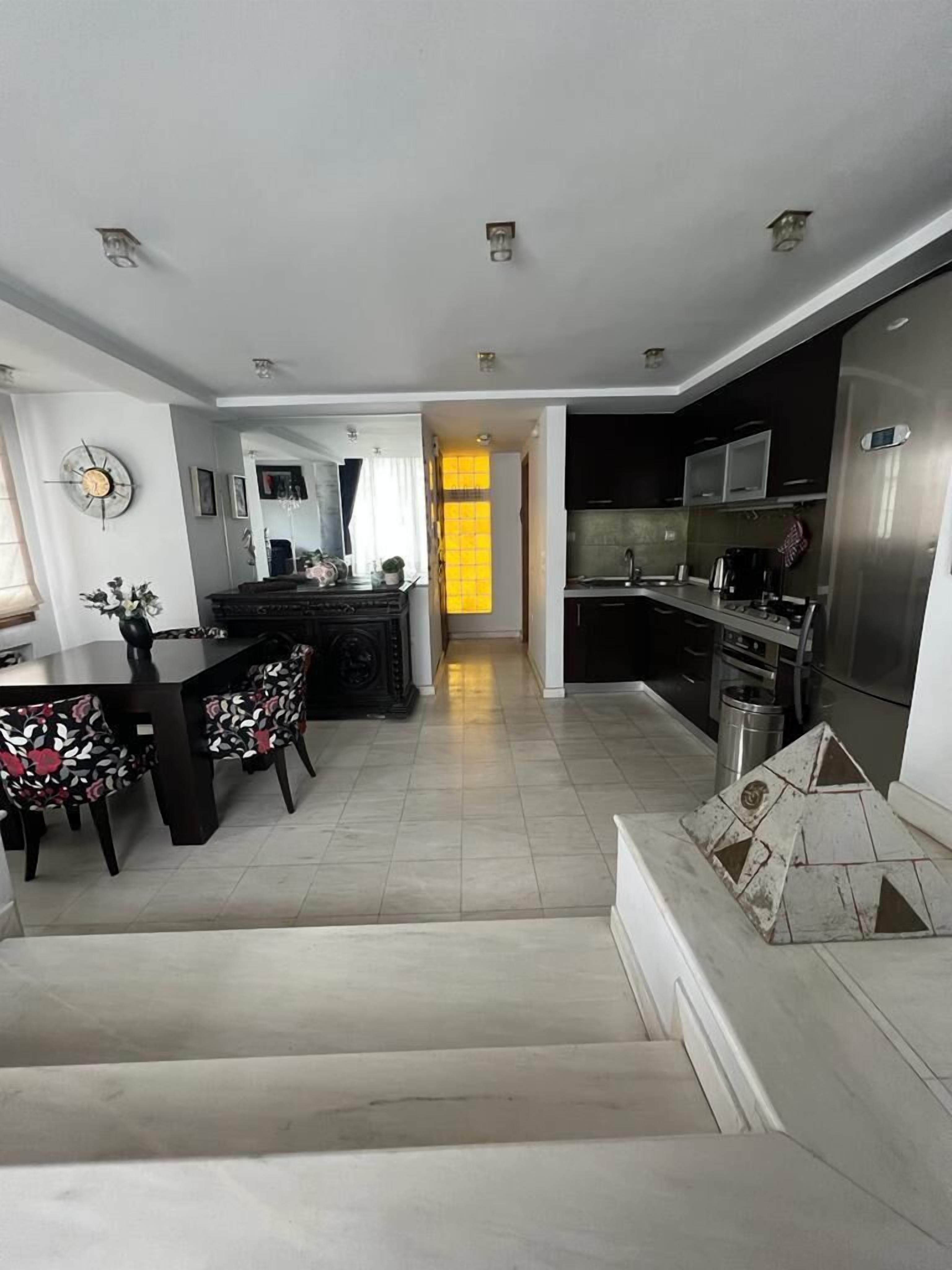 A modern kitchen with stainless steel appliances, a dining area with a black table and floral chairs, and a staircase leading to another level.
