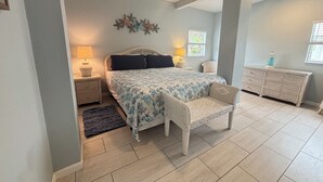 Een slaapkamer met een bed, nachtkastjes, een stoel, een dressoir en decoratieve wandkunst.