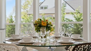 A dining table set for six with clear glassware and a centerpiece, in a room with large windows and a view of a house. - Luxury 3 King Suite Retreat 3 Blocks to Downtown! (Carlton)
