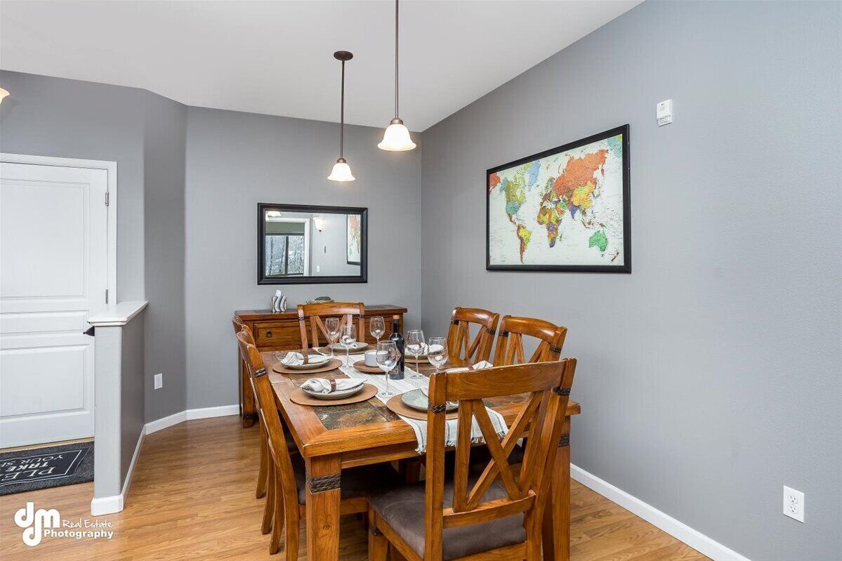 A dining area with a wooden table set for six, a world map on the wall, and pendant lights.