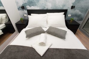 A neatly made bed with white and gray pillows, a rolled white towel, and a gray throw blanket. - Hostel Cool (Split)