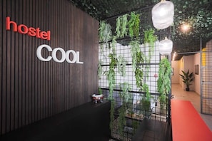 A modern hostel interior with vertical wooden panels, a 'hostel cool' sign, hanging plants, and a red carpet. - Hostel Cool (Split)
