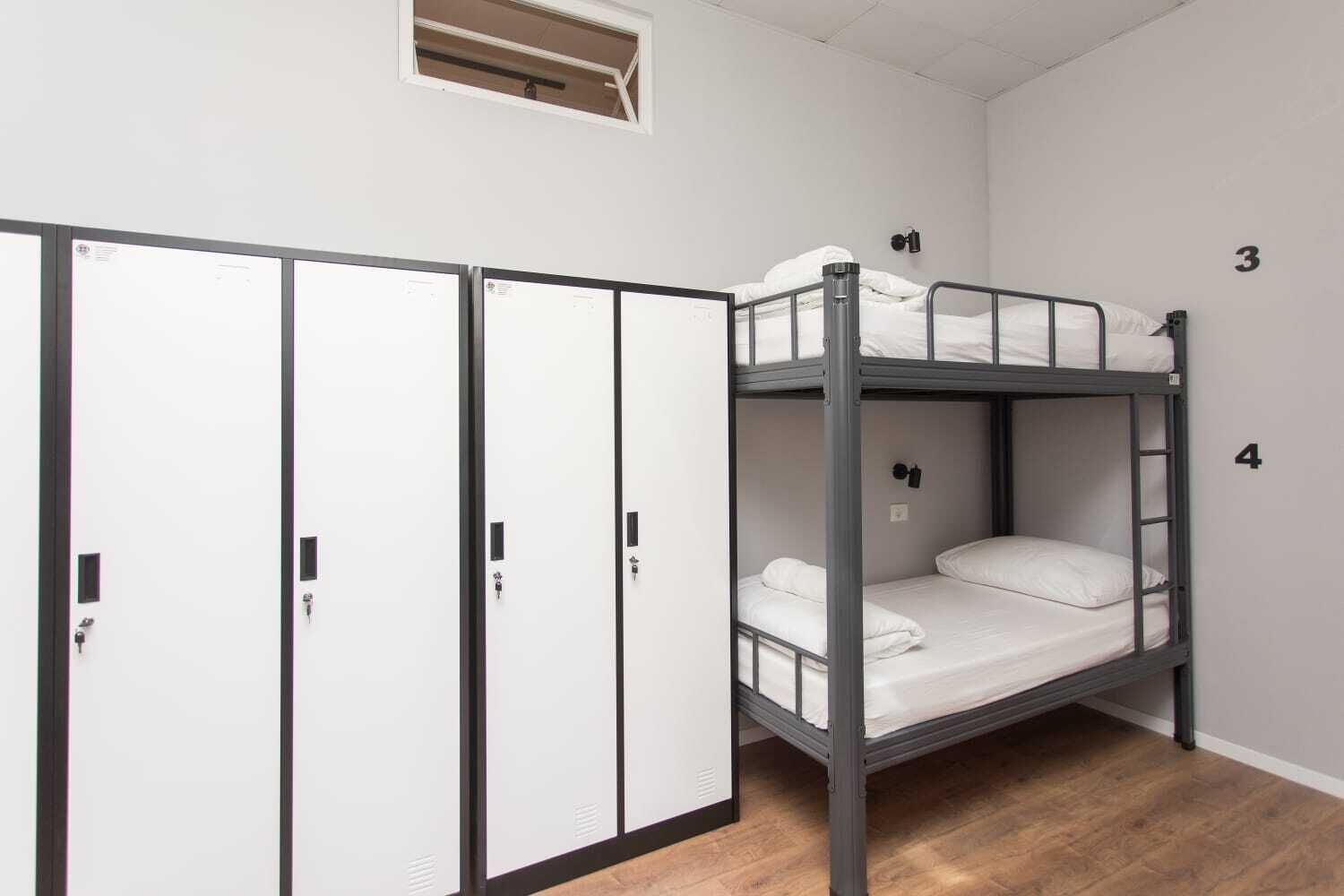 Una cama litera de dos plazas, un armario con dos puertas y una ventana pequeña sobre la cama.
