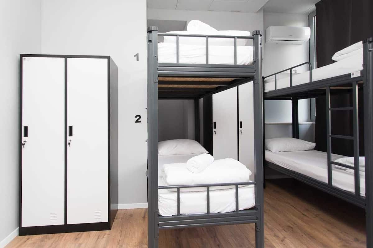 A dormitory room with bunk beds, a wardrobe, and a window.