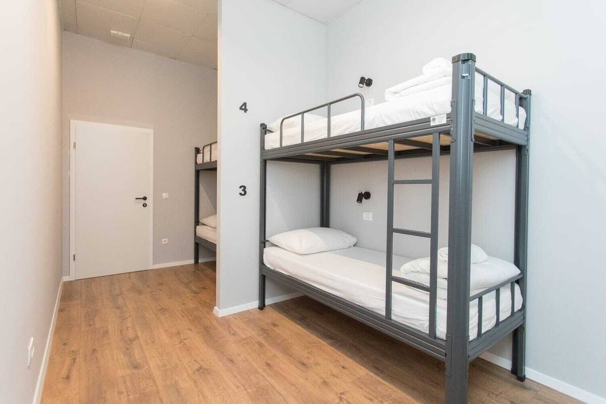 A dormitory room with bunk beds, a wooden floor, and a door.