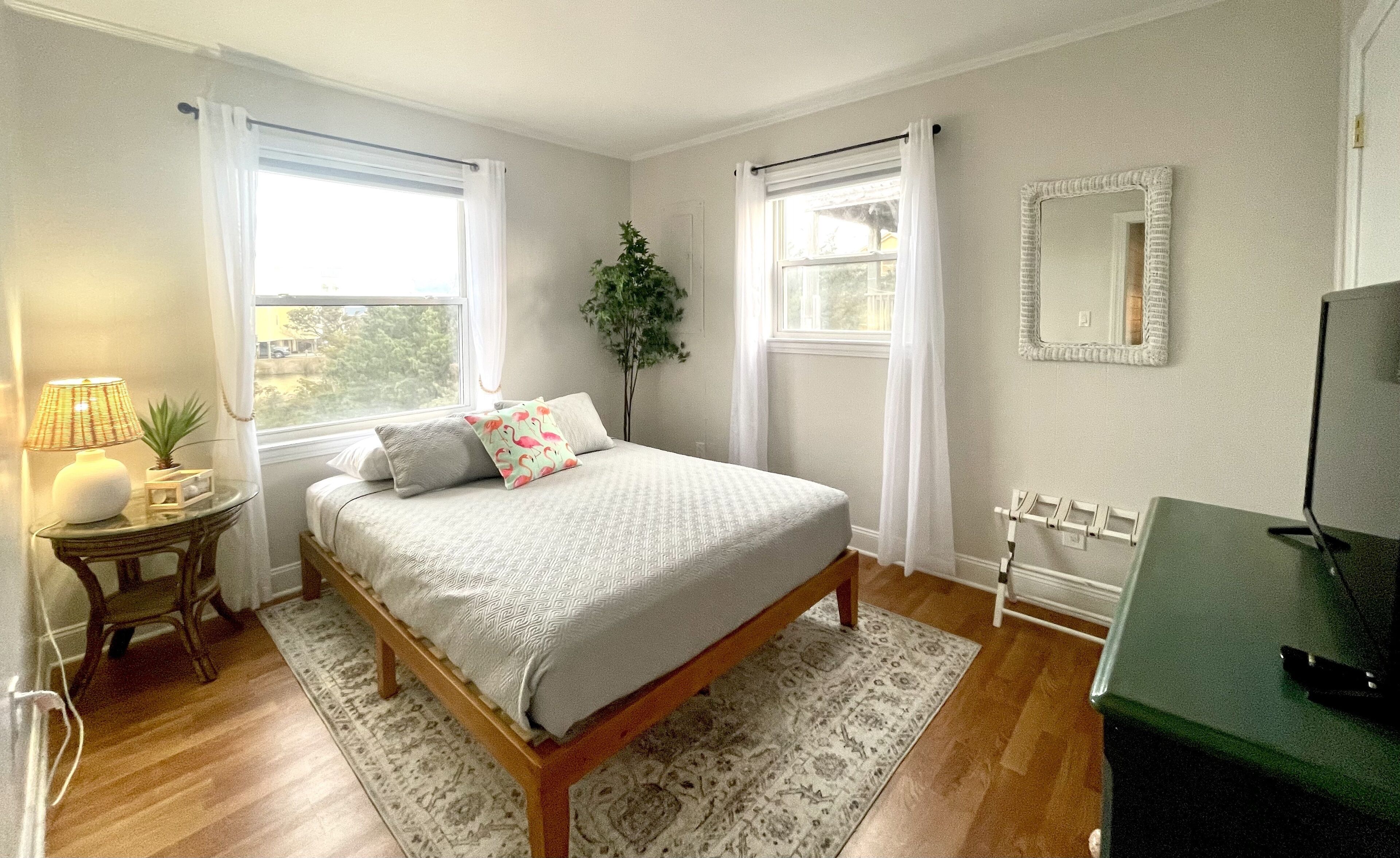 A bedroom with a bed, a bedside table with a lamp, a mirror, and a TV.