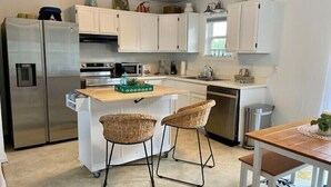 Una cocina compacta con armarios blancos, un refrigerador de acero inoxidable, una isla de madera con taburetes y un lavavajillas.