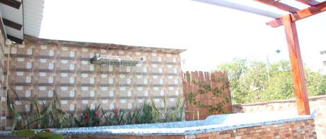 A brick patio with a tiled edge, a pergola structure, and a brick wall with a water feature.