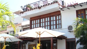 An outdoor patio with tables and chairs, surrounded by potted plants and a white building with a balcony. - Hotel Rodadero Dorado (Santa Marta)