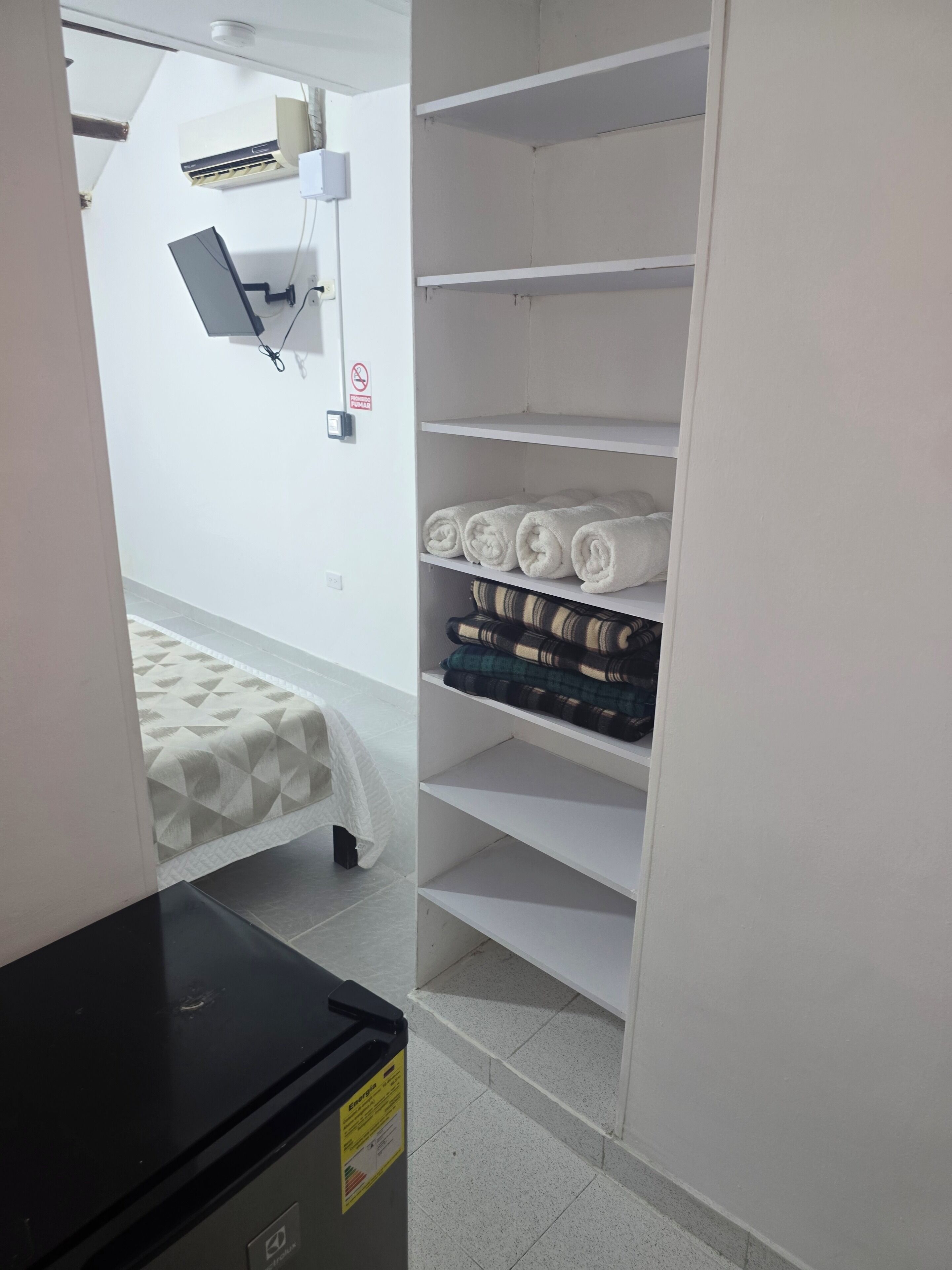 Una habitación de hotel con una cama, un escritorio, un armario blanco y un pequeño cubo de basura.