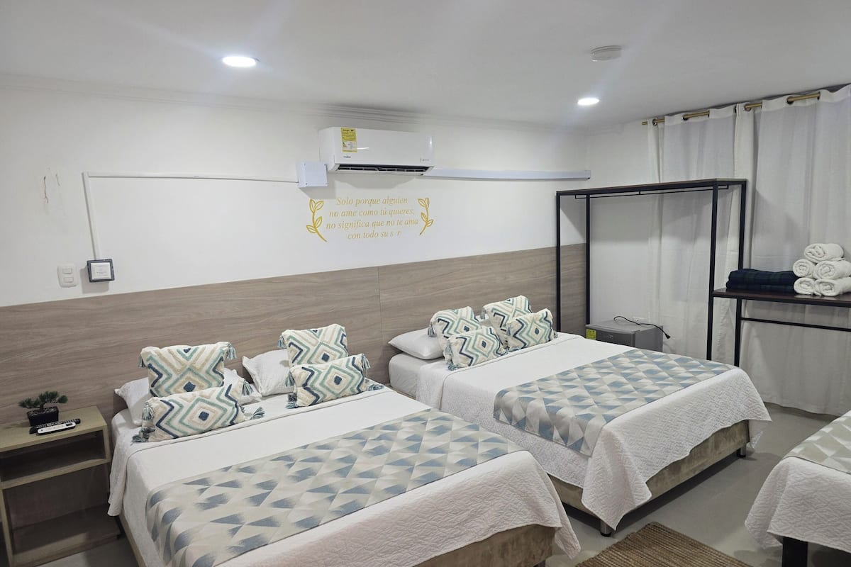 A hotel room with two beds, a bedside table, a nightstand, a mirror, a wardrobe, and a wall-mounted air conditioner.