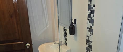 A bathroom with a wooden door, a white sink, a toilet, and a glass partition.