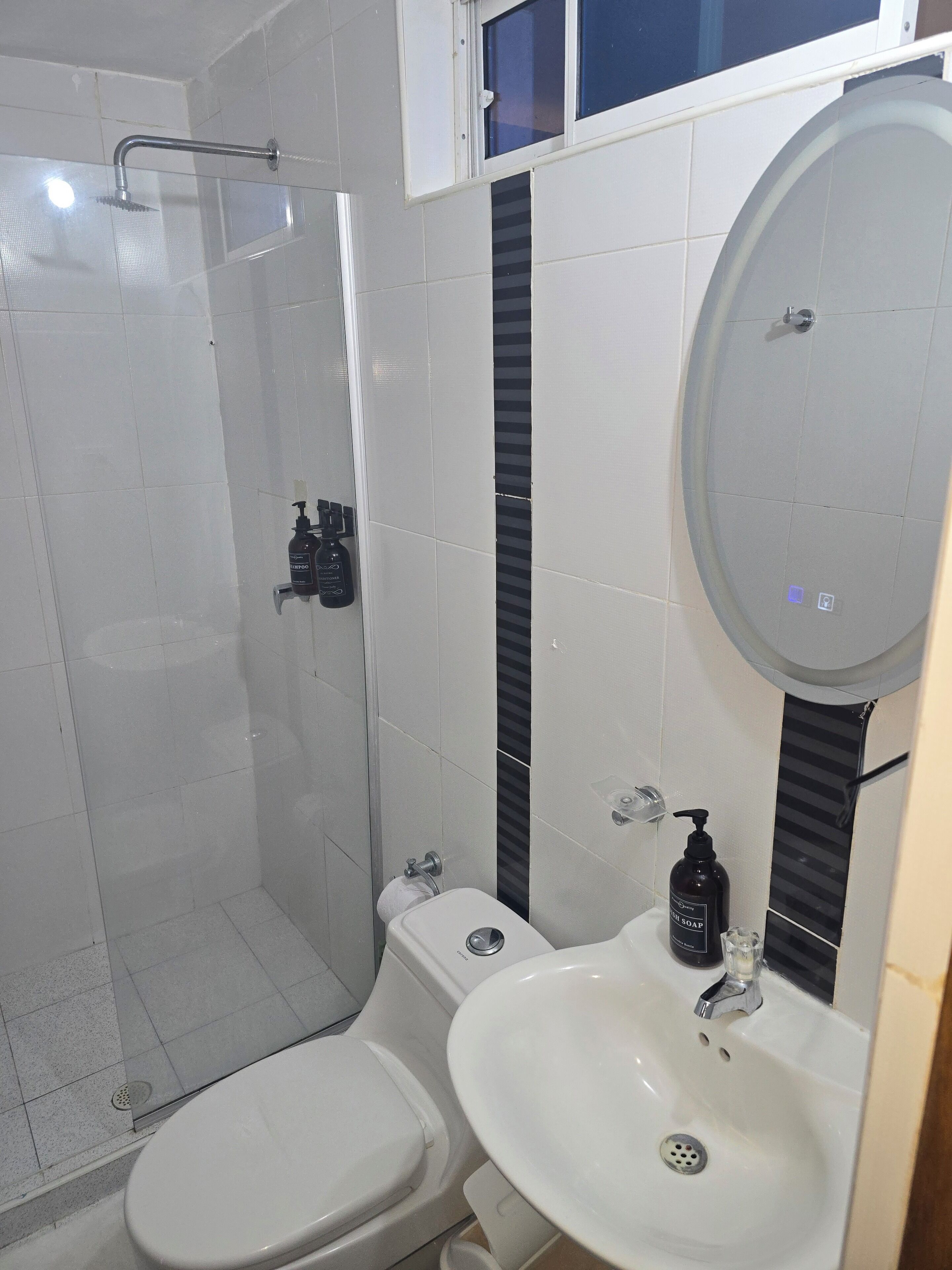 Un baño con cabina de ducha de vidrio, inodoro y lavamanos con espejo.