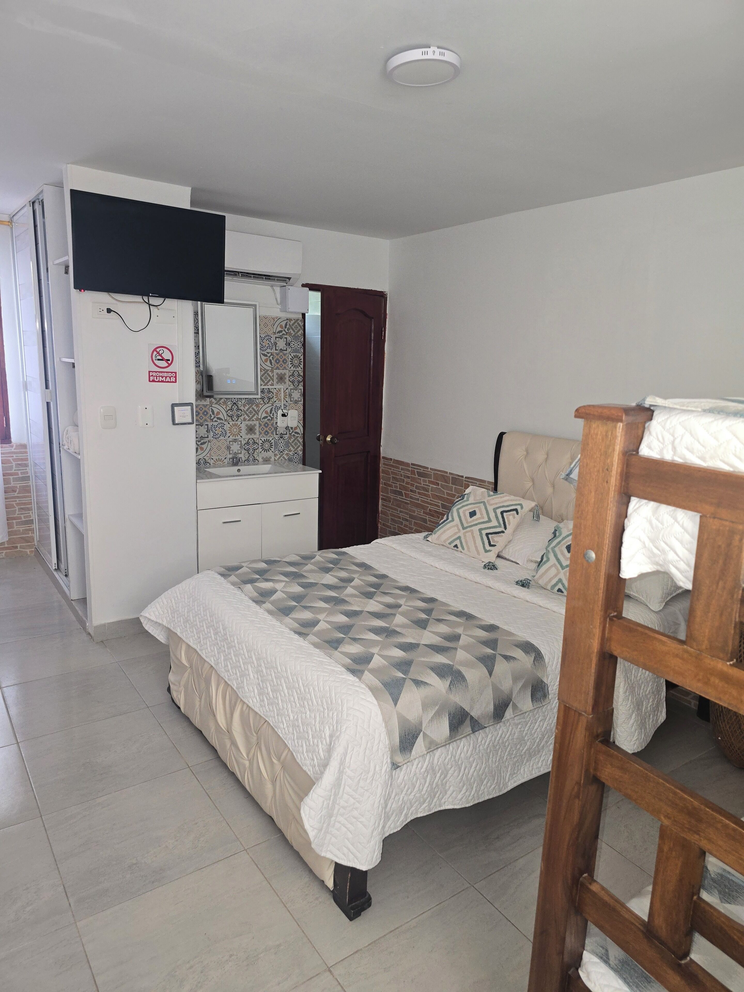A bedroom with a bed, a wardrobe, a television, and a bathroom with a tiled wall.